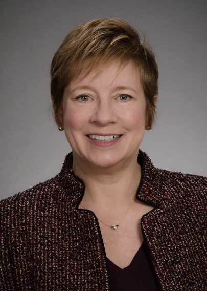 Gail smiles at the camera wearing a brown collared jacket