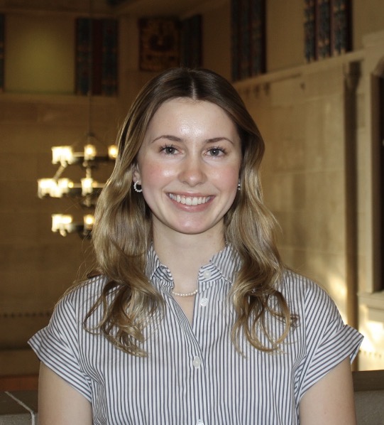 Abby looks at the camera wearing a black and white stripped button up shirt.