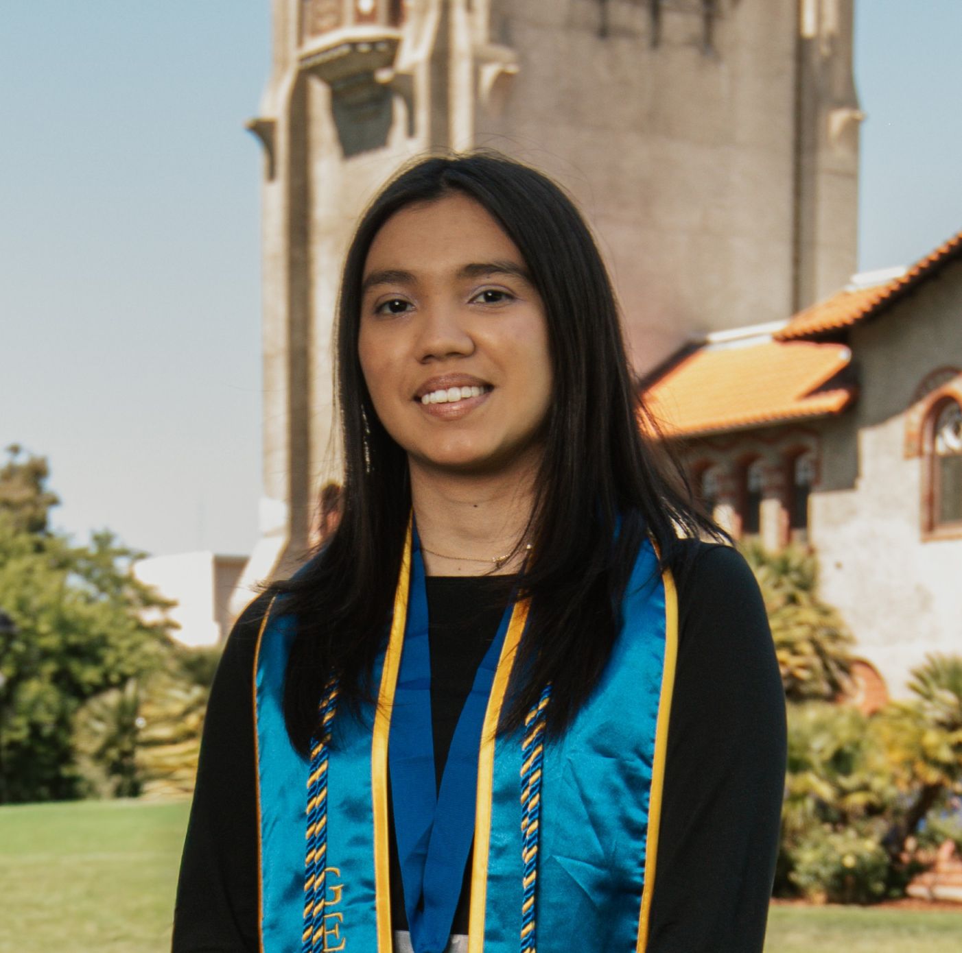 Ashely looks at the camera wearing a black sweater and a blue graduation sash and tassel.