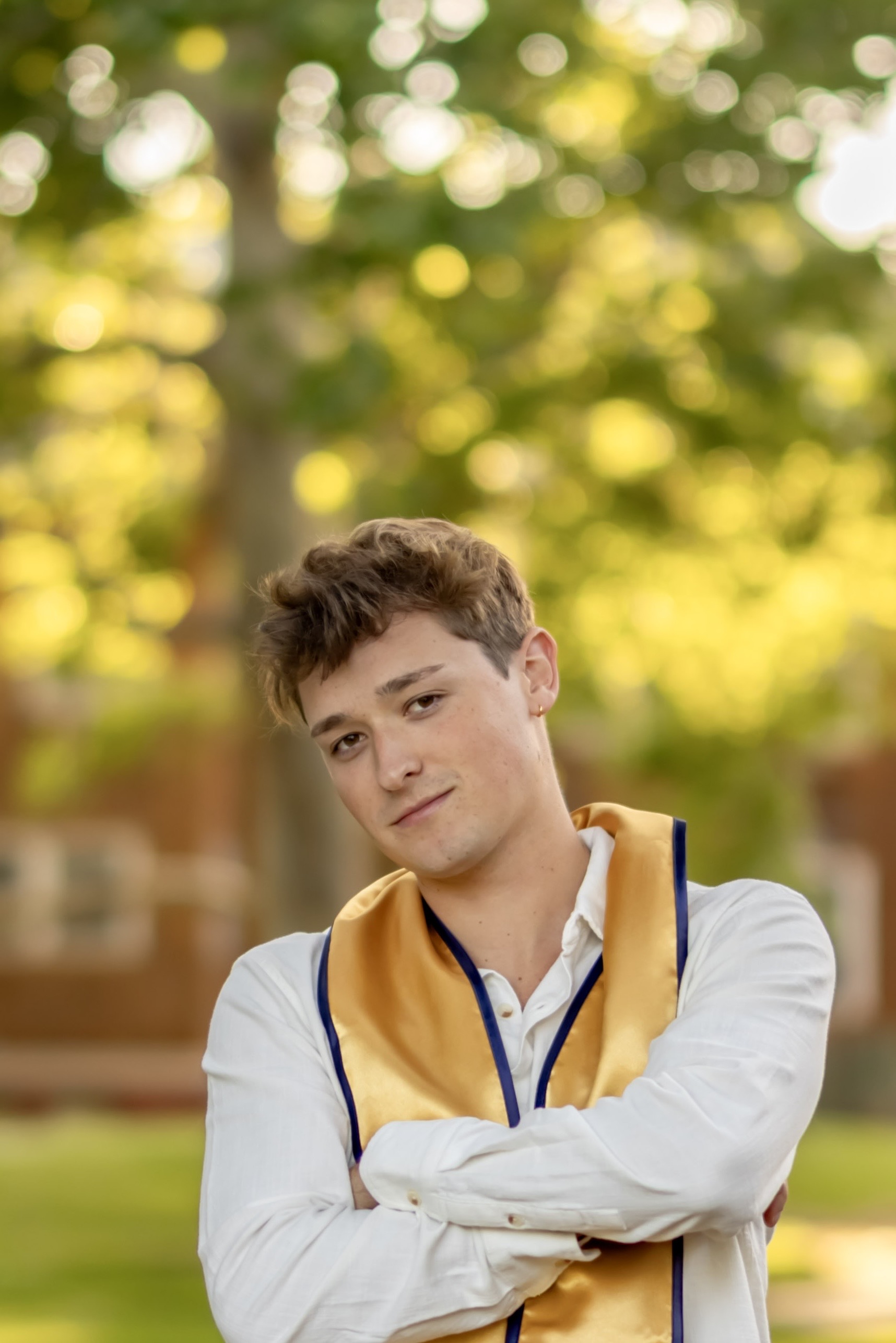 Jack looks at the camera wearing a white button up shirt and a golden graduation sash.