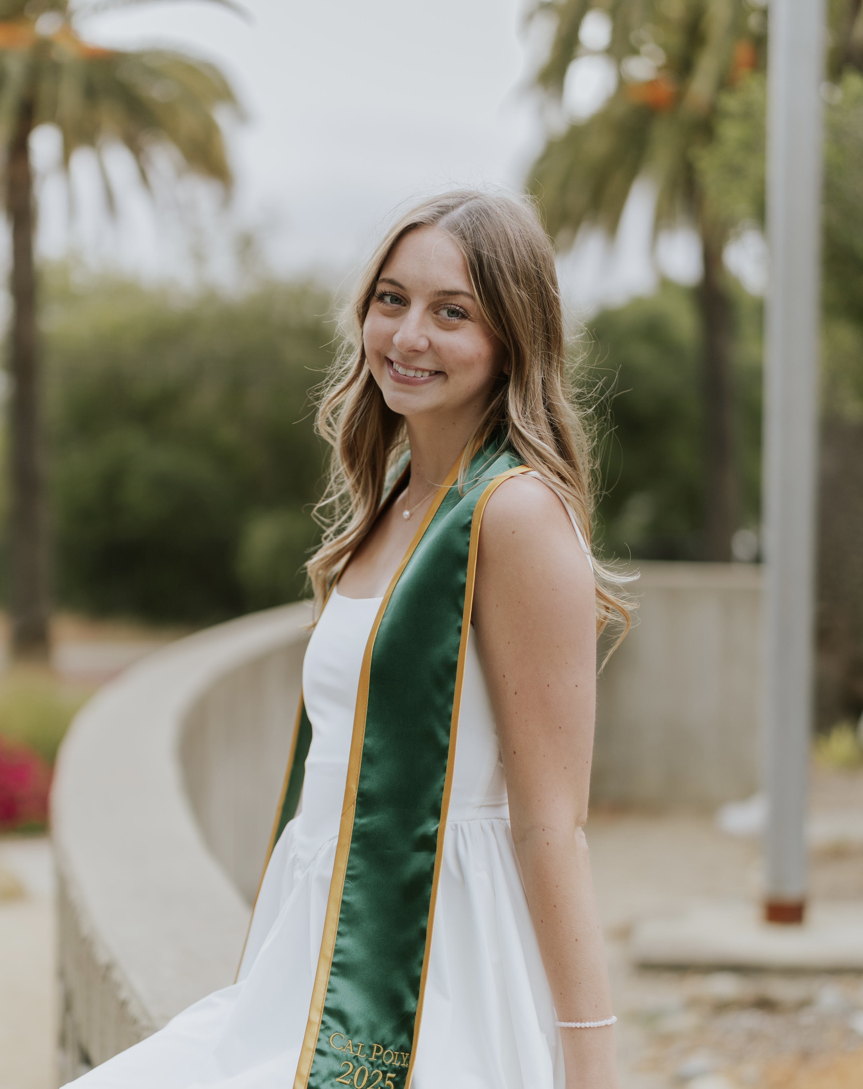Olivia looks at the camera wearing a white dress and a green graduation sash.